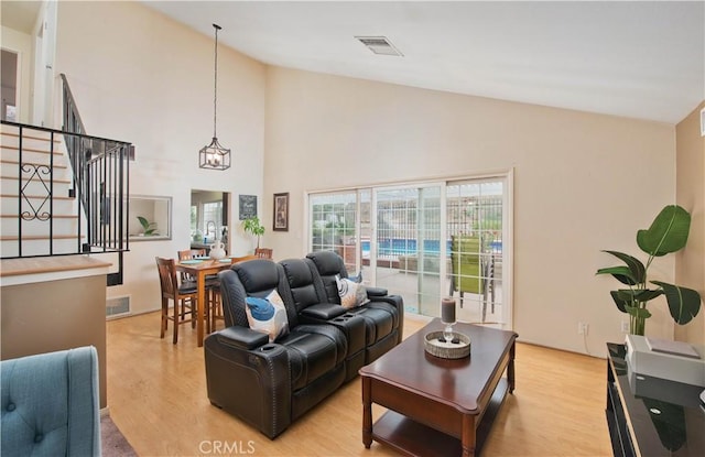 living room with light wood-type flooring, high vaulted ceiling, and a notable chandelier