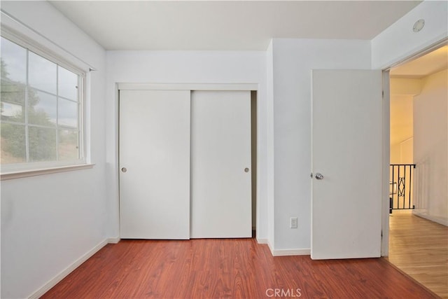 unfurnished bedroom with a closet, hardwood / wood-style flooring, and multiple windows