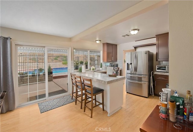 kitchen featuring a kitchen bar, kitchen peninsula, stainless steel fridge with ice dispenser, and a healthy amount of sunlight