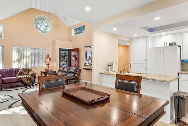 dining space featuring sink, high vaulted ceiling, and light hardwood / wood-style floors