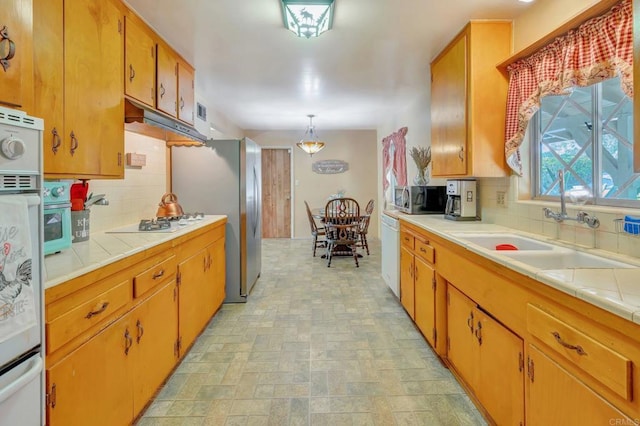 kitchen featuring pendant lighting, sink, backsplash, stainless steel appliances, and tile counters