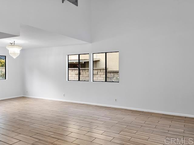 empty room with a wealth of natural light, a chandelier, and light wood-type flooring