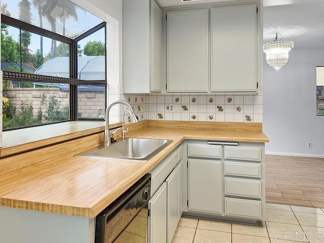 kitchen with backsplash, a notable chandelier, black dishwasher, and sink