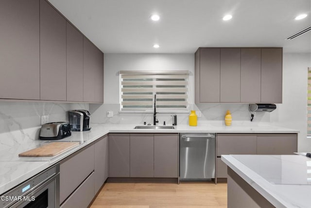 kitchen featuring dishwasher, sink, gray cabinetry, decorative backsplash, and light hardwood / wood-style floors