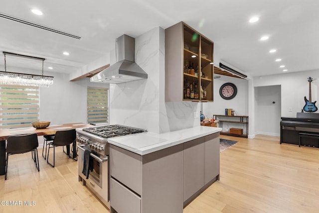 kitchen featuring high end stainless steel range oven, decorative light fixtures, ventilation hood, and light wood-type flooring