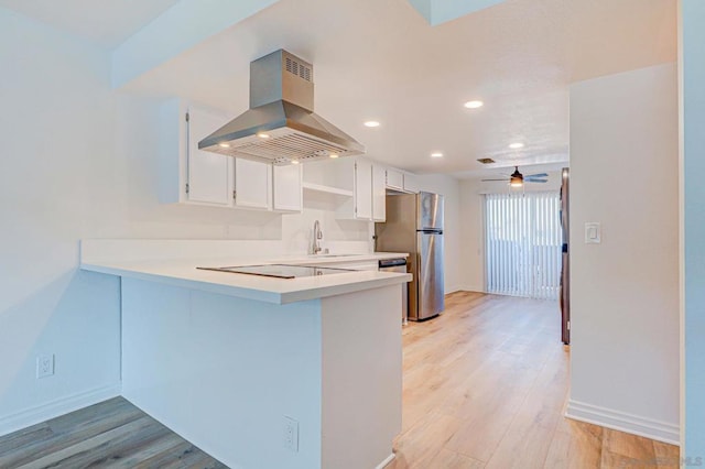 kitchen featuring kitchen peninsula, stainless steel fridge, light hardwood / wood-style flooring, white cabinetry, and range hood