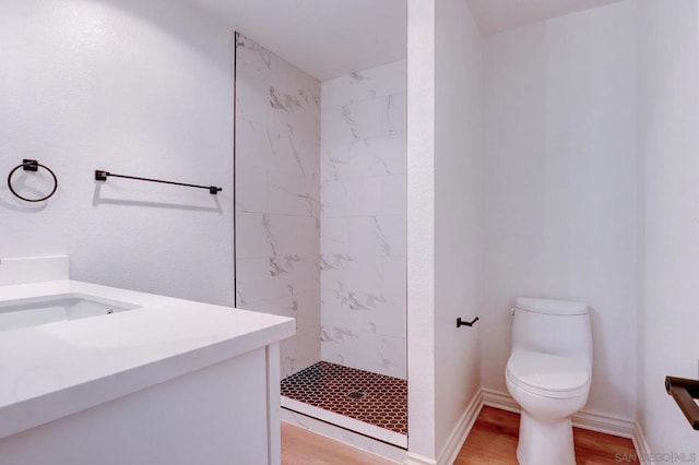 bathroom featuring a tile shower, hardwood / wood-style floors, vanity, and toilet