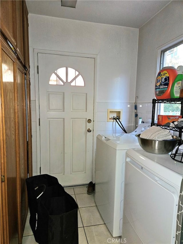 clothes washing area featuring cabinets, tile walls, washer and clothes dryer, and light tile patterned flooring