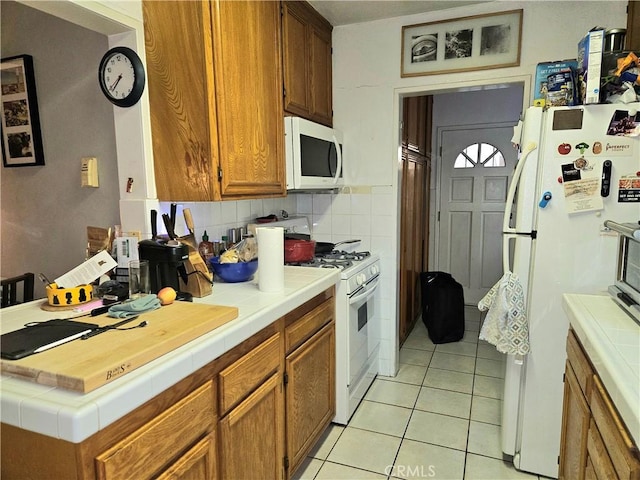 kitchen with decorative backsplash, light tile patterned floors, white appliances, and tile countertops