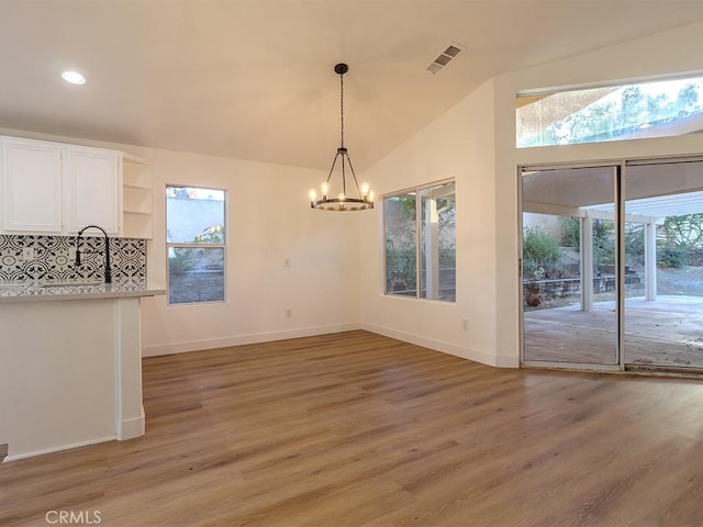 unfurnished dining area with hardwood / wood-style floors, vaulted ceiling, and a notable chandelier