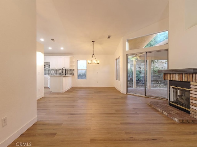 unfurnished living room featuring sink, an inviting chandelier, light hardwood / wood-style floors, vaulted ceiling, and a fireplace