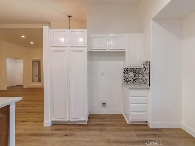 kitchen with backsplash, white cabinets, hanging light fixtures, and light wood-type flooring