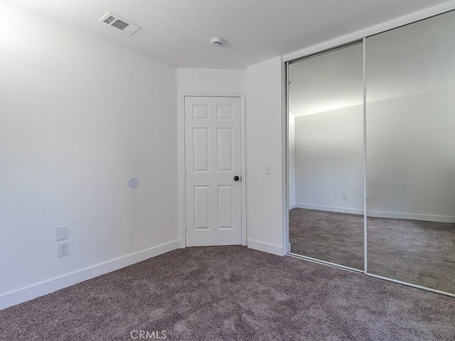 unfurnished bedroom with dark carpet and a closet