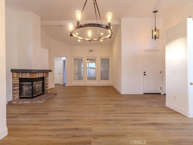 unfurnished living room featuring a fireplace, an inviting chandelier, and light wood-type flooring