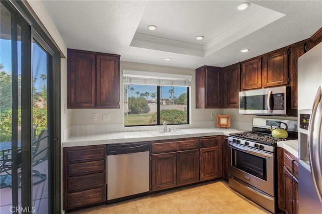 kitchen with sink, stainless steel appliances, crown molding, a tray ceiling, and light tile patterned floors