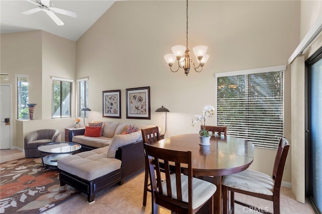 dining area with ceiling fan with notable chandelier, a healthy amount of sunlight, light tile patterned floors, and high vaulted ceiling