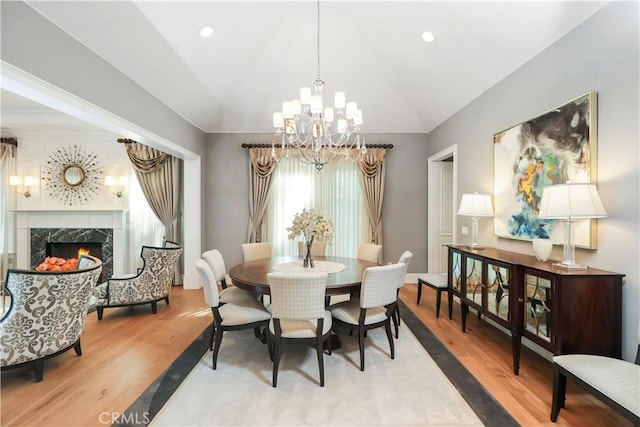 dining area featuring a premium fireplace, a chandelier, vaulted ceiling, and hardwood / wood-style flooring