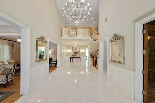 hall with light hardwood / wood-style flooring, an inviting chandelier, a high ceiling, and ornamental molding