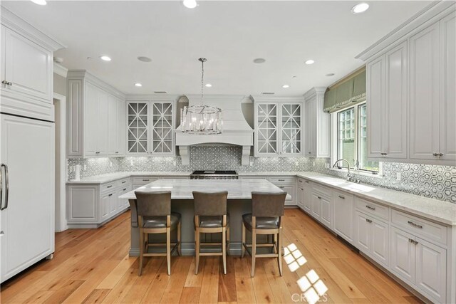 kitchen with light wood-type flooring, paneled refrigerator, light stone counters, pendant lighting, and a center island