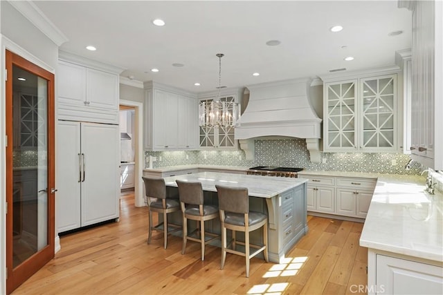 kitchen featuring a kitchen island, premium range hood, paneled built in fridge, white cabinets, and light wood-type flooring