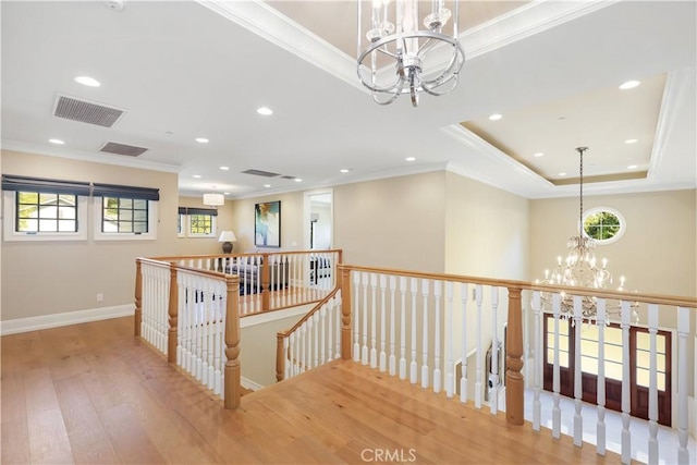 corridor with a raised ceiling, hardwood / wood-style flooring, crown molding, and a notable chandelier