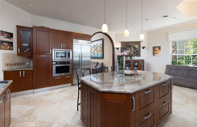 kitchen with built in appliances, light stone countertops, decorative light fixtures, a breakfast bar, and a center island