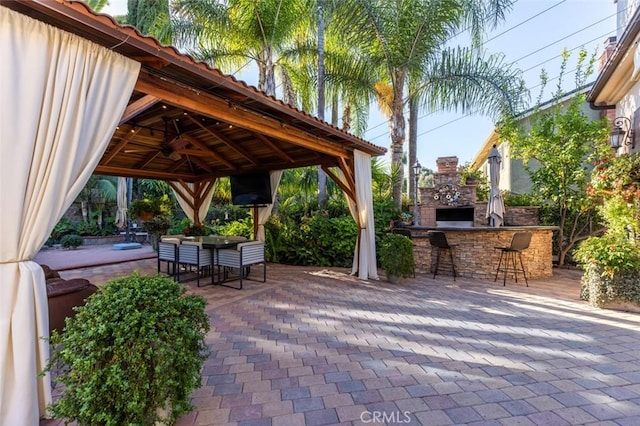 view of patio with ceiling fan, a gazebo, and an outdoor stone fireplace