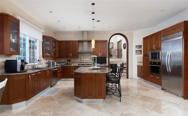 kitchen with built in appliances, sink, a center island, dark stone counters, and hanging light fixtures