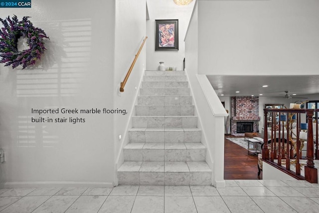 staircase with ceiling fan and a brick fireplace