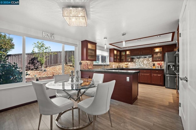 dining space with light wood-type flooring, a chandelier, a raised ceiling, and plenty of natural light