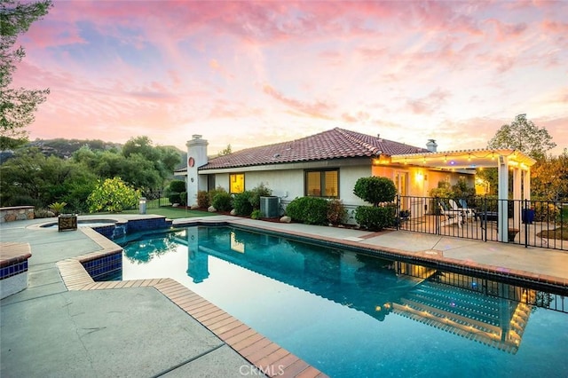 pool at dusk featuring central AC unit, a patio area, and an in ground hot tub