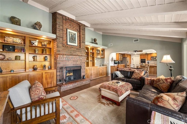 living room featuring ceiling fan, a brick fireplace, built in features, lofted ceiling with beams, and wood-type flooring