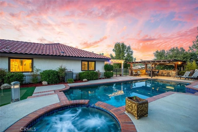 pool at dusk with a pergola, an in ground hot tub, and a patio