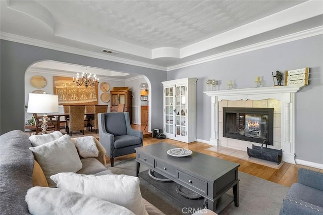 living room with a raised ceiling, a fireplace, crown molding, and hardwood / wood-style floors