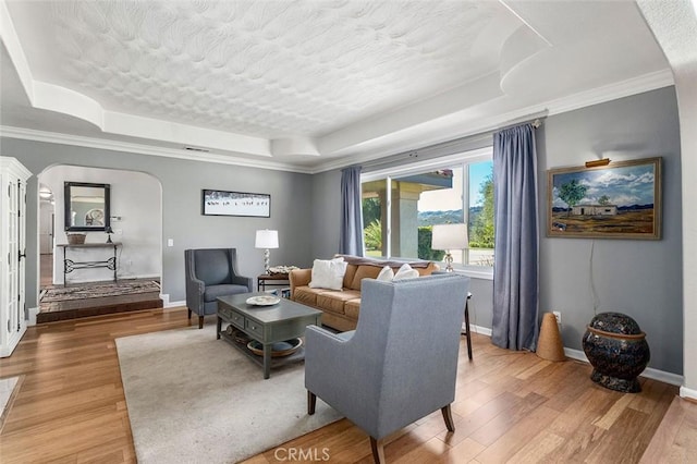 living room with a raised ceiling, crown molding, wood-type flooring, and a textured ceiling