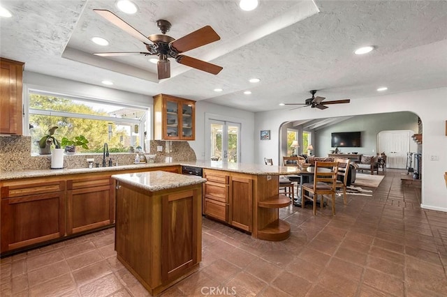 kitchen featuring decorative backsplash, a textured ceiling, a center island, and ceiling fan