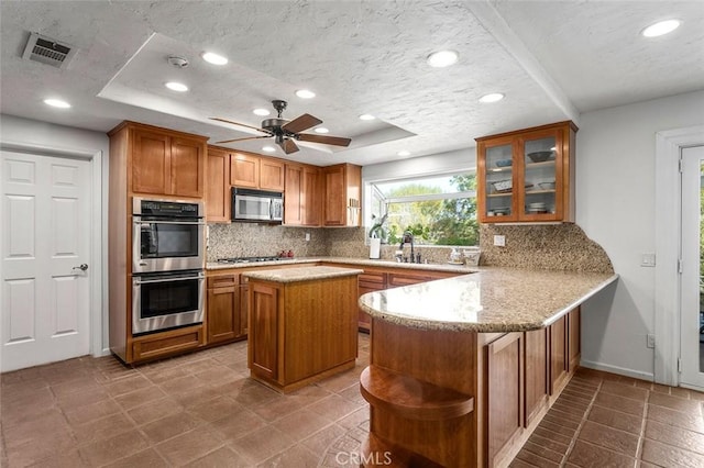 kitchen featuring a center island, kitchen peninsula, stainless steel appliances, and a tray ceiling