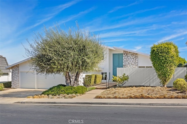 mid-century modern home with an attached garage, fence, concrete driveway, stone siding, and stucco siding