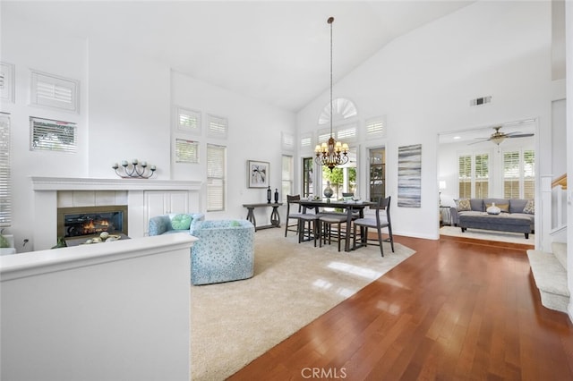 living room with hardwood / wood-style floors, ceiling fan with notable chandelier, high vaulted ceiling, and a tiled fireplace