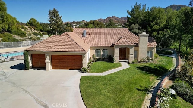 mediterranean / spanish-style house featuring a mountain view, a fenced in pool, a garage, and a front yard