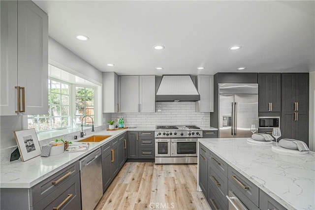 kitchen featuring gray cabinetry, sink, built in appliances, wall chimney exhaust hood, and light hardwood / wood-style floors