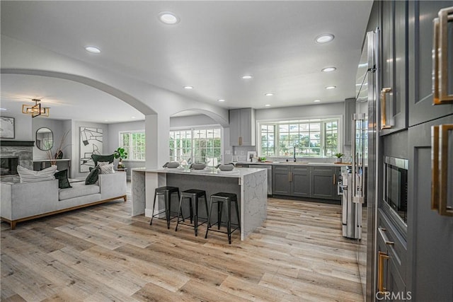 kitchen with gray cabinetry, sink, a kitchen breakfast bar, light hardwood / wood-style flooring, and a center island with sink