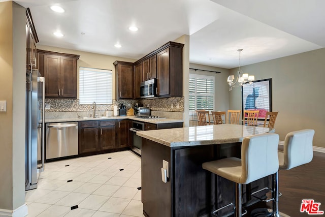 kitchen with decorative backsplash, light stone counters, stainless steel appliances, sink, and an inviting chandelier