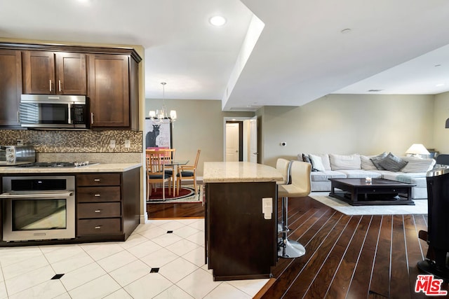 kitchen featuring light stone countertops, a chandelier, pendant lighting, a kitchen bar, and appliances with stainless steel finishes