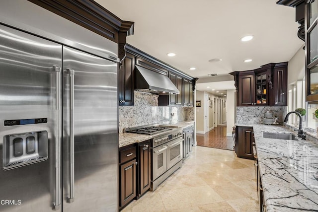 kitchen featuring dark brown cabinetry, light stone countertops, sink, wall chimney exhaust hood, and high quality appliances