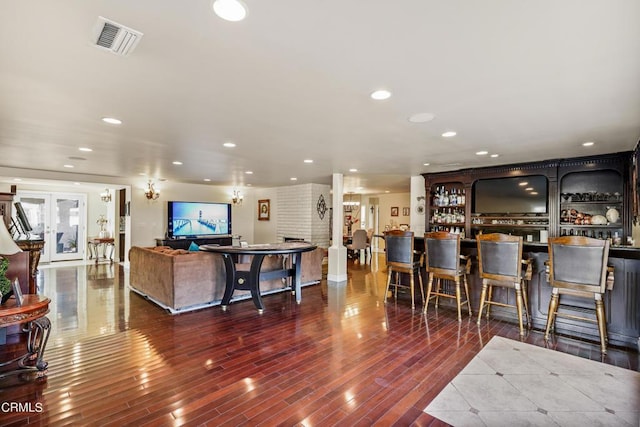 living room with bar area, decorative columns, and wood-type flooring