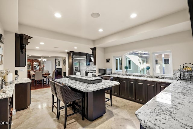 kitchen featuring a kitchen bar, appliances with stainless steel finishes, light stone countertops, dark brown cabinets, and an inviting chandelier