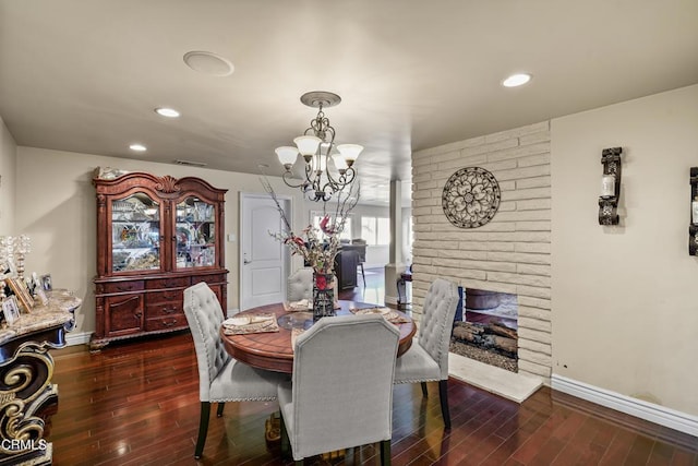 dining area featuring dark hardwood / wood-style flooring, a brick fireplace, and a notable chandelier