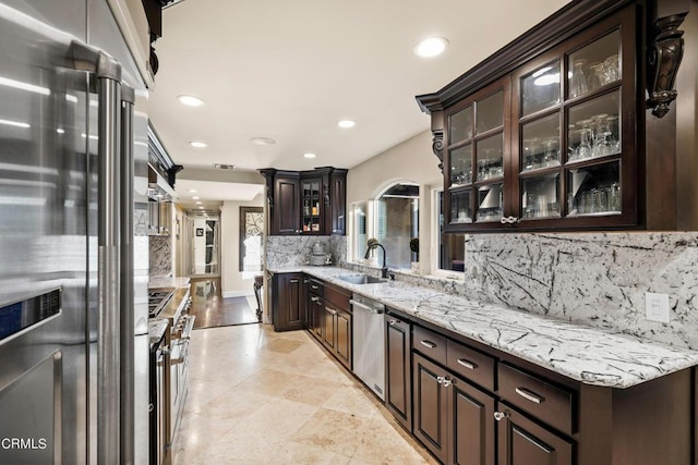 kitchen with decorative backsplash, light stone countertops, dark brown cabinetry, premium appliances, and sink