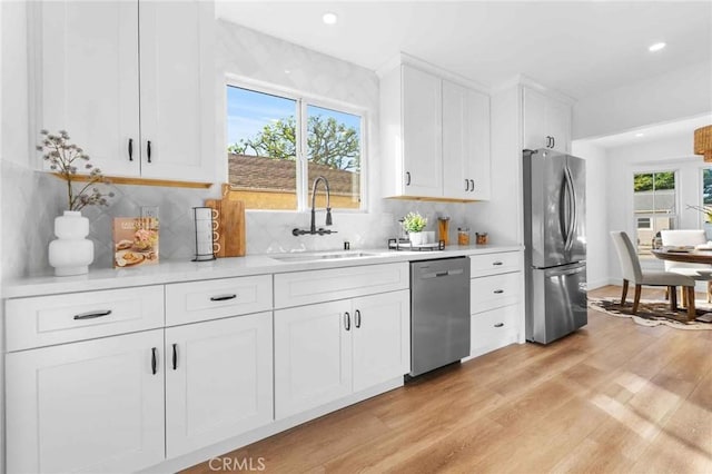 kitchen with appliances with stainless steel finishes, light wood-type flooring, sink, white cabinetry, and plenty of natural light